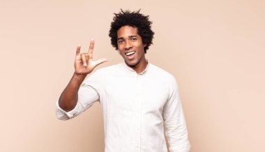 Genç siyah afro adam mutlu, eğlenceli, kendinden emin, pozitif ve asi hissediyor, elle kaya ya da heavy metal işareti yapıyor.