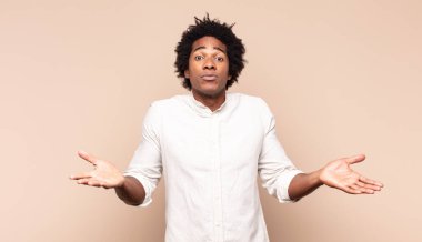 Genç siyah afro adam şaşkın ve şaşkın hissediyor, doğru cevap veya karardan emin değil, bir seçim yapmaya çalışıyor.