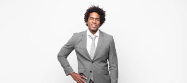 Siyah afro iş adamı mutlu bir şekilde gülümsüyor, eli kalçasında ve kendinden emin, olumlu, gururlu ve arkadaş canlısı.