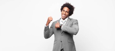 Siyah afro iş adamı neşeli bir şekilde gülümsüyor ve yan taraftaki fotokopi alanını işaret ediyor, mutlu ve tatmin olmuş hissediyor.