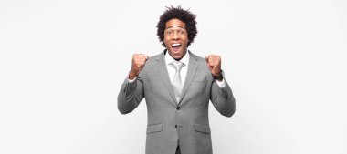 Siyah afro iş adamı kızgın bir ifadeyle saldırganca bağırıyor ya da yumruklarıyla başarıyı kutluyor.
