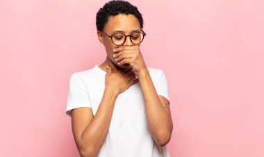 Afro genç siyahi kadın boğazı ağrıyormuş ve grip belirtileri gösteriyormuş, ağzı kapalı öksürüyormuş.