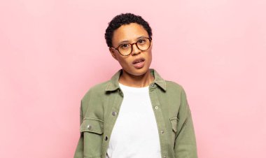 afro young black woman feeling puzzled and confused, with a dumb, stunned expression looking at something unexpected
