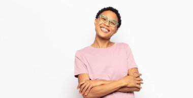 Afro genç siyah kadın kollarını kavuşturup mutlu bir şekilde gülüyor, rahat, pozitif ve tatmin olmuş bir poziyonla.