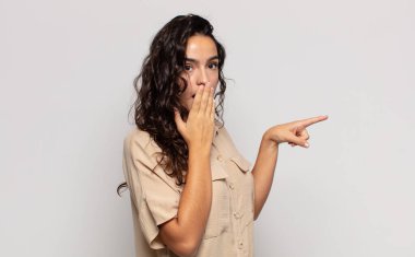 Güzel genç bir kadın kendini mutlu, şok olmuş ve şaşırmış hissediyor. Ağzını eliyle kapatıyor ve yanal kopya alanını işaret ediyor.