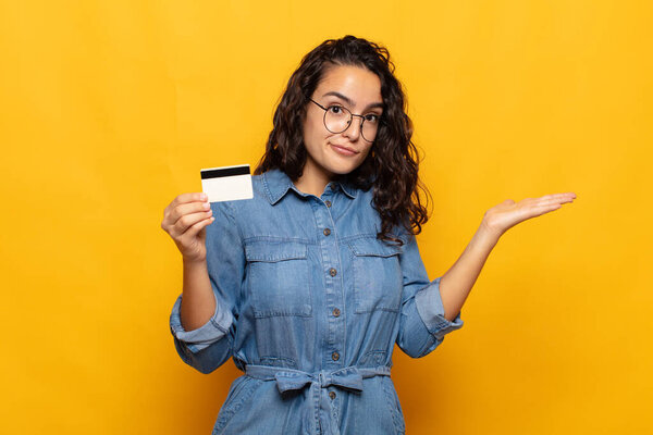 молодая латиноамериканка чувствует себя озадаченной и смущенной, сомневаясь, взвешивая или выбирая различные варианты со смешным выражением лица