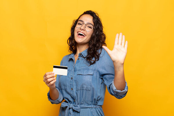 молодая латиноамериканка, счастливо и весело улыбающаяся, машущая рукой, приветствуя и приветствуя вас, или прощаясь