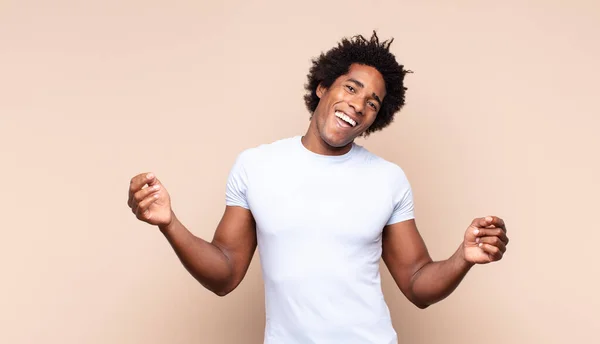 young black afro man smiling happily with funny face, joking and looking through peephole, spying on secrets