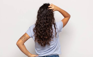 Güzel genç bir kadın bilgisiz ve kafası karışık hissediyor, bir çözüm düşünüyor, eli kalçasında, diğeri kafasında, dikiz aynasından.