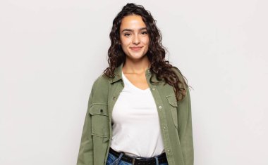 Güzel, genç bir bayan pozitif ve kendinden emin gülümsüyor. Tatmin olmuş, arkadaş canlısı ve mutlu görünüyor.