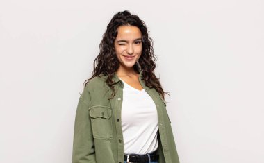 Güzel genç bayan mutlu ve arkadaş canlısı görünüyor, gülümsüyor ve sana olumlu bir tavırla göz kırpıyor.