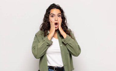 Güzel genç bir kadın şok olmuş ve korkmuş hissediyor, ağzı açık ve elleri yanaklarında korkmuş görünüyor.