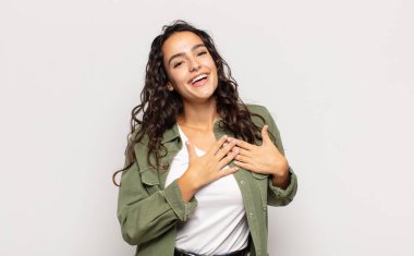 Güzel genç bir kadın romantik, mutlu ve aşık, neşeyle gülümsüyor ve kalbe yakın el ele tutuşuyor.