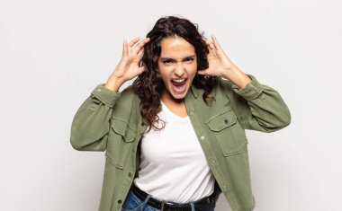 Güzel genç bir kadın panik ya da öfke içinde bağırıyor, şok olmuş, korkmuş ya da öfkeli, elleri başının yanında.