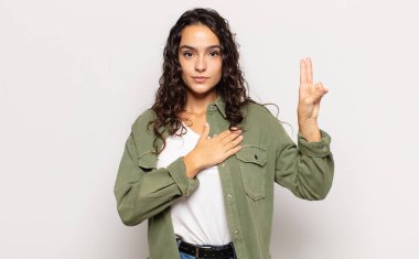 Güzel, genç bir kadın mutlu, kendinden emin ve güvenilir görünüyor, gülümsüyor ve zafer işareti gösteriyor, olumlu bir tavırla.