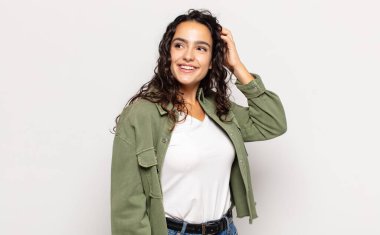 Güzel genç bir kadın neşeli ve sıradan bir şekilde gülümsüyor, olumlu, mutlu ve kendinden emin bir bakışla göğüs göğüse tutuşuyor.