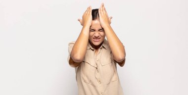 Güzel genç bir kadın stresli ve endişeli, depresif ve hayal kırıklığına uğramış hissediyor, iki elini de başa kaldırıyor.