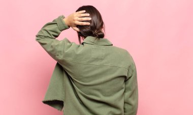 Güzel genç bir kadın düşünüyor ya da şüphe ediyor, kafasını kaşıyor, kafası karışık ve kafası karışık hissediyor, geriye ya da arkaya bakıyor.