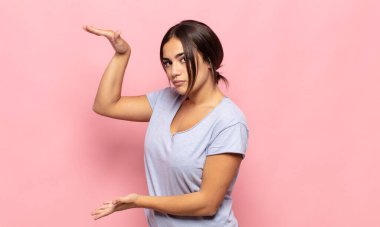 Güzel genç bir kadın iki eli de yan tarafında fotokopi alanı olan bir nesneyi tutuyor, bir nesneyi gösteriyor, sunuyor ya da reklamını yapıyor.