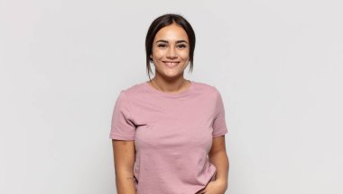 Çapraz kollarla kameraya gülümseyen güzel genç bir kadın ve mutlu, kendinden emin, tatmin olmuş bir ifade, yan görüş.