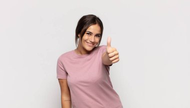 Güzel genç bir kadın gururlu, kaygısız, kendinden emin ve mutlu, başparmağıyla olumlu gülümsüyor.