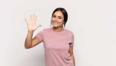 Güzel genç bir bayan gülümsüyor ve arkadaş canlısı görünüyor, 5 ya da 5 numarayı gösteriyor, elleri önde, geriye doğru sayıyor.