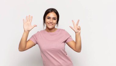 Güzel genç bir bayan gülümsüyor ve arkadaş canlısı görünüyor, 8 ya da 8 numarayı gösteriyor, elleri önde, geri sayıyor.