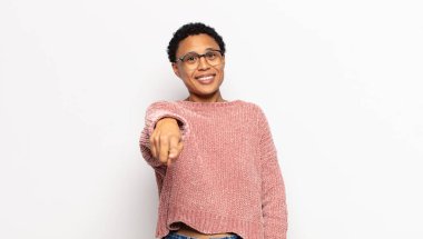 Genç afro kadın kameraya tatmin olmuş, kendinden emin, dost canlısı bir gülümsemeyle bakıyor ve seni seçiyor.