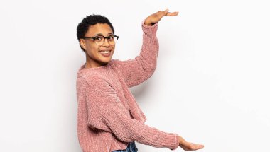 Genç afro kadın gülümsüyor, mutlu, pozitif ve tatmin olmuş hissediyor, fotokopi alanında nesne veya konsept tutuyor veya gösteriyor