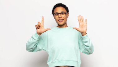 Genç afro kadın gülümsüyor ve arkadaş canlısı görünüyor, 7 ya da 7 numarayı gösteriyor, eli önde, geriye doğru sayıyor.