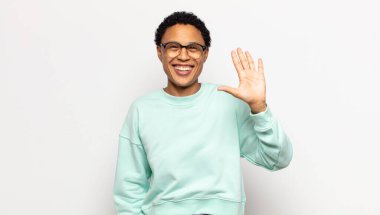 Genç afro kadın gülümsüyor ve arkadaş canlısı görünüyor, 5 ya da 5 numarayı gösteriyor, eli önde, geriye doğru sayıyor.