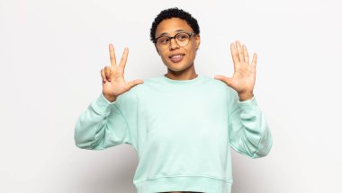 Genç afro kadın gülümsüyor ve arkadaş canlısı görünüyor, 8 ya da 8 numarayı gösteriyor, elleri önde, geriye doğru sayıyor.