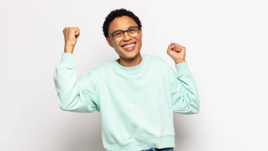 Genç afro kadın muzaffer bir şekilde bağırıyor, heyecanlı, mutlu ve şaşırmış görünüyor, kutlama yapıyor.