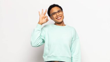 Genç afro kadın kendini başarılı ve tatmin olmuş hissediyor, ağzı açık gülümsüyor, elle işaret veriyor.