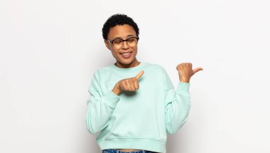 Genç afro kadın neşeyle gülümsüyor ve yan taraftaki fotokopi alanını gösteriyor, mutlu ve tatmin olmuş hissediyor.