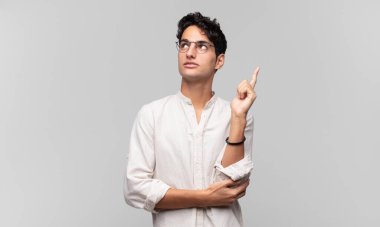 Genç yakışıklı adam mutlu bir şekilde gülümsüyor ve yan bakıyor, merak ediyor, düşünüyor ya da bir fikri var.