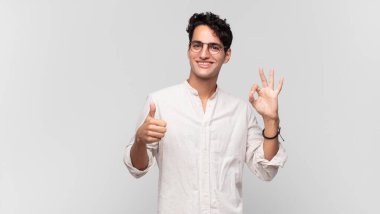 Genç yakışıklı adam kendini mutlu, şaşkın, tatmin olmuş ve şaşırmış hissediyor, tamam gösteriyor ve el kol hareketleri yapıyor, gülümsüyor.