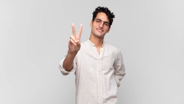 Genç yakışıklı adam gülümsüyor ve mutlu görünüyor, kaygısız ve olumlu, zafer veya barış işareti yapıyor.