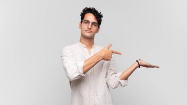 Genç yakışıklı adam gülümsüyor, mutlu, tasasız ve tatmin olmuş hissediyor, fotokopi alanındaki konsepte ya da fikre işaret ediyor.