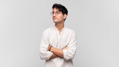 Genç yakışıklı adam omuz silkiyor, kafası karışık ve kararsız, kolları bağlı ve şaşkın görünüyor.