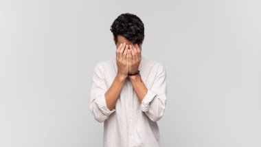 Genç yakışıklı adam üzgün, hayal kırıklığına uğramış, gergin ve depresif, iki eliyle yüzünü kaplayan, ağlayan