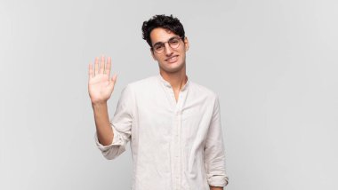 Genç yakışıklı adam mutlu ve neşeyle gülümsüyor, el sallıyor, seni selamlıyor ve selamlıyor, ya da hoşça kal diyor.