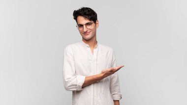 Genç yakışıklı adam neşeyle gülümsüyor, mutlu hissediyor ve fotokopi uzayında bir konsept gösteriyor.