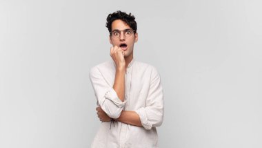 Genç yakışıklı adam şok ve inançsızlık içinde, elleri yanak ve kolları çapraz, sersemlemiş ve şaşırmış hissediyor.