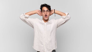 Genç yakışıklı adam heyecanlı ve şaşırmış görünüyor, ağzı açık, elleri başının üstünde, şanslı bir kazanan gibi hissediyor.