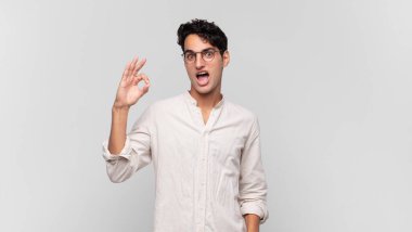 Genç yakışıklı adam kendini başarılı ve tatmin olmuş hissediyor, ağzı açık gülümsüyor, elle işaret veriyor.