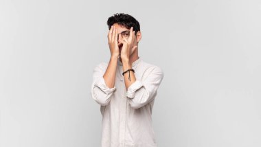 Genç ve yakışıklı bir adam korkmuş ya da utanmış hissediyor. Gözleri yarı kapalı ya da ellerle dikizliyor ya da dikizliyor.