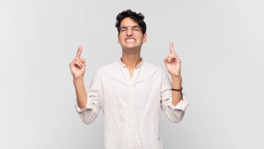 Genç yakışıklı adam gülümsüyor ve endişeyle iki parmağını çapraz yapıyor. Endişeli ve iyi şanslar diliyor.