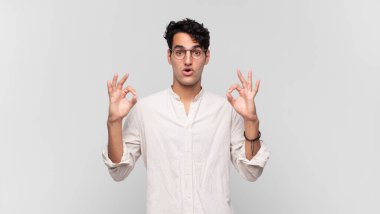 Genç yakışıklı adam şok olmuş, şaşırmış ve şaşırmış hissediyor. Onaylıyor. İki eliyle de onay işareti yapıyor.