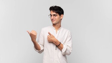 Genç yakışıklı adam neşeyle gülümsüyor ve yan taraftaki fotokopi alanını gösteriyor, mutlu ve tatmin olmuş hissediyor.